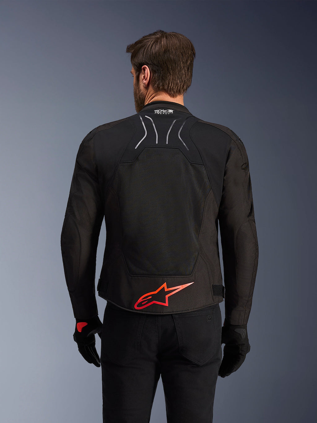 Alpinestars SMX Air Jacke, Rückansicht, Schwarz mit leuchtend rotem Alpinestars-Logo am unteren Rücken, mit High-Airflow-Tech-Mesh-Einsatz und Tech-Air-Ready-Branding, getragen von einem männlichen Fahrer mit schwarzer Hose und Handschuhen