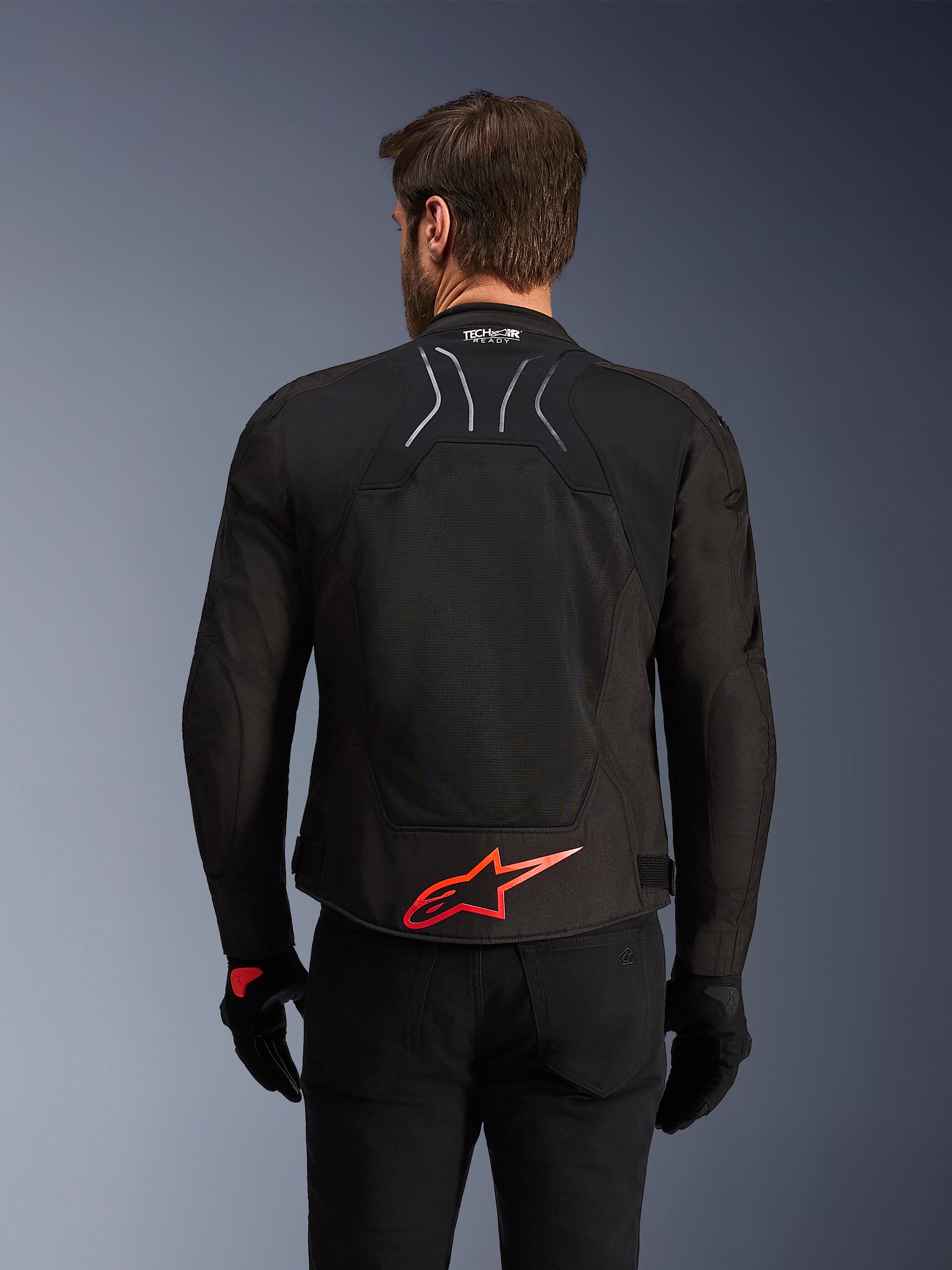 Alpinestars SMX Air Jacke, Rückansicht, Schwarz mit leuchtend rotem Alpinestars-Logo am unteren Rücken, mit High-Airflow-Tech-Mesh-Einsatz und Tech-Air-Ready-Branding, getragen von einem männlichen Fahrer mit schwarzer Hose und Handschuhen