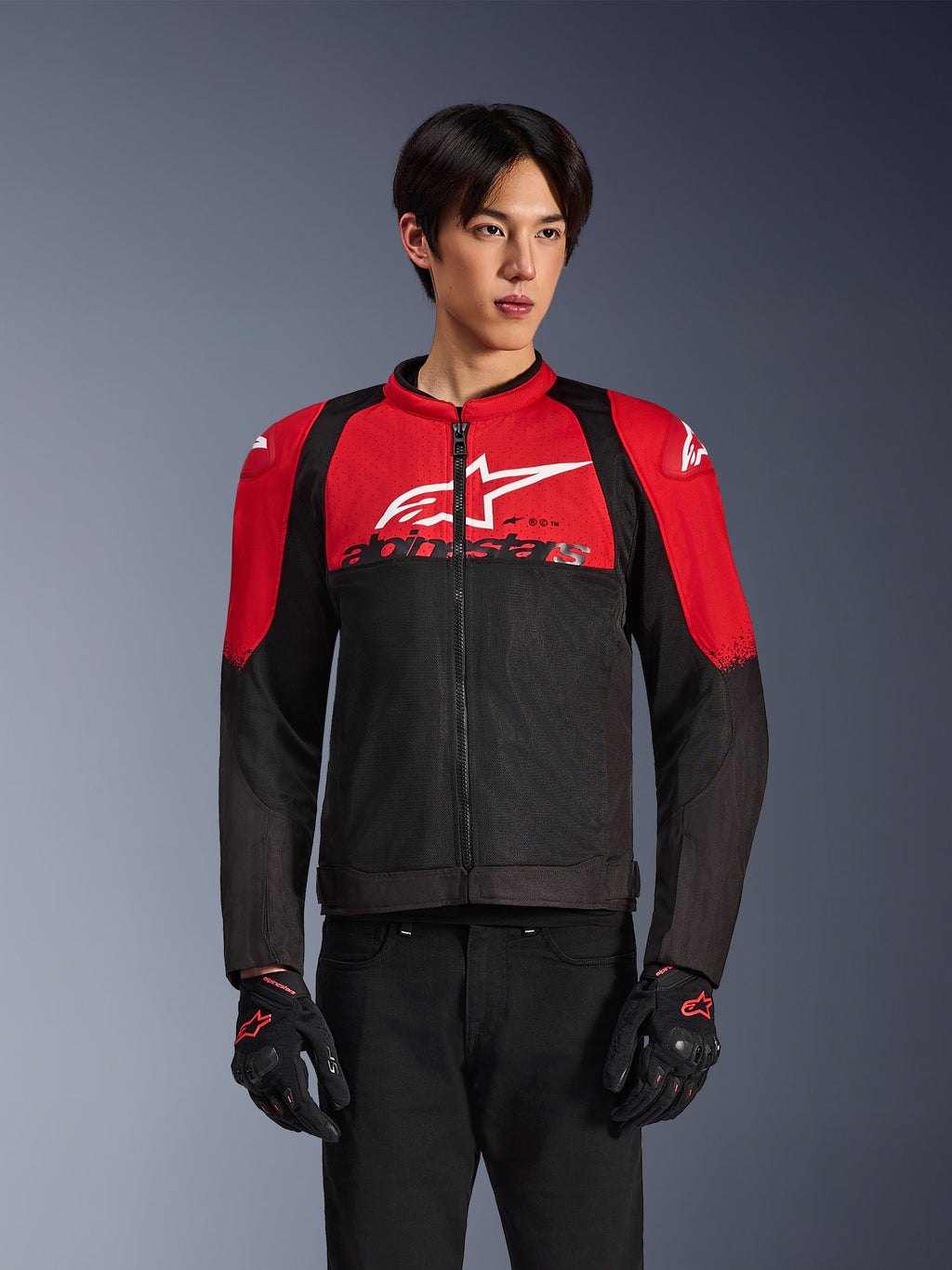 Alpinestars SMX Air Jacke, Motorrad-Mesh-Jacke, leuchtendes Rot und Schwarz, getragen von einem Modell mit schwarzen Motorradhandschuhen, mit großem weißem Logo auf der Brust, belüftete Textilkonstruktion mit roten Schulterpartien und schwarzen Ärmeln, sportliche Performance-Ausrüstung für Fahrten bei warmem Wetter