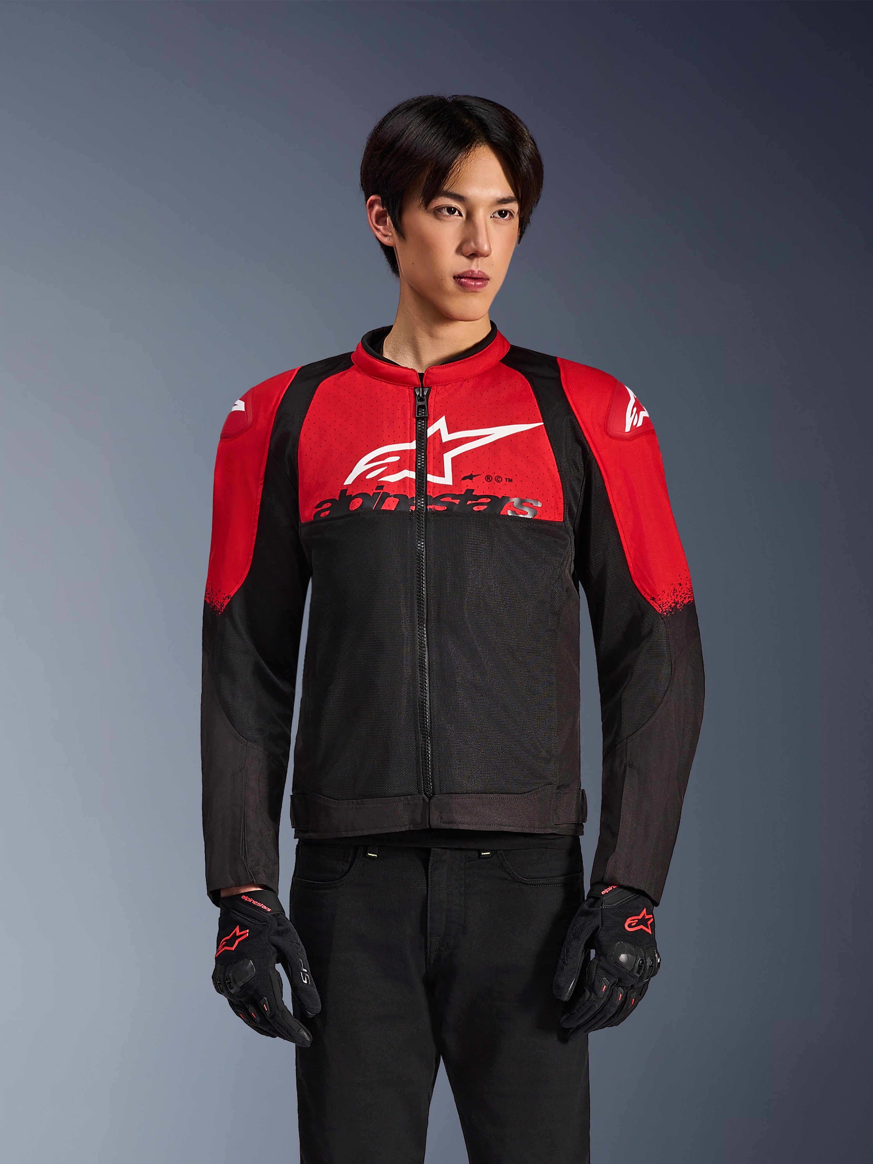 Alpinestars SMX Air Jacke, Motorrad-Mesh-Jacke, leuchtendes Rot und Schwarz, getragen von einem Modell mit schwarzen Motorradhandschuhen, mit großem weißem Logo auf der Brust, belüftete Textilkonstruktion mit roten Schulterpartien und schwarzen Ärmeln, sportliche Performance-Ausrüstung für Fahrten bei warmem Wetter