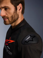 Alpinestars SMX Air Jacke, Schwarz und Rot, Nahaufnahme des DFS Lite Schulterprotektors mit Stern-Logo, getragen von einem bärtigen Mann, Textil-Renn- und Sport-Motorradjacke.