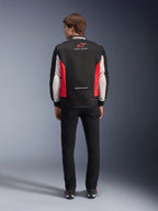 Alpinestars Monza Sport Jacket, Black Bright Red and White textile motorcycle jacket, rear view shown on a model, featuring red star logo and 'ASTARS' collar branding with slogans, worn with black pants and riding boots.