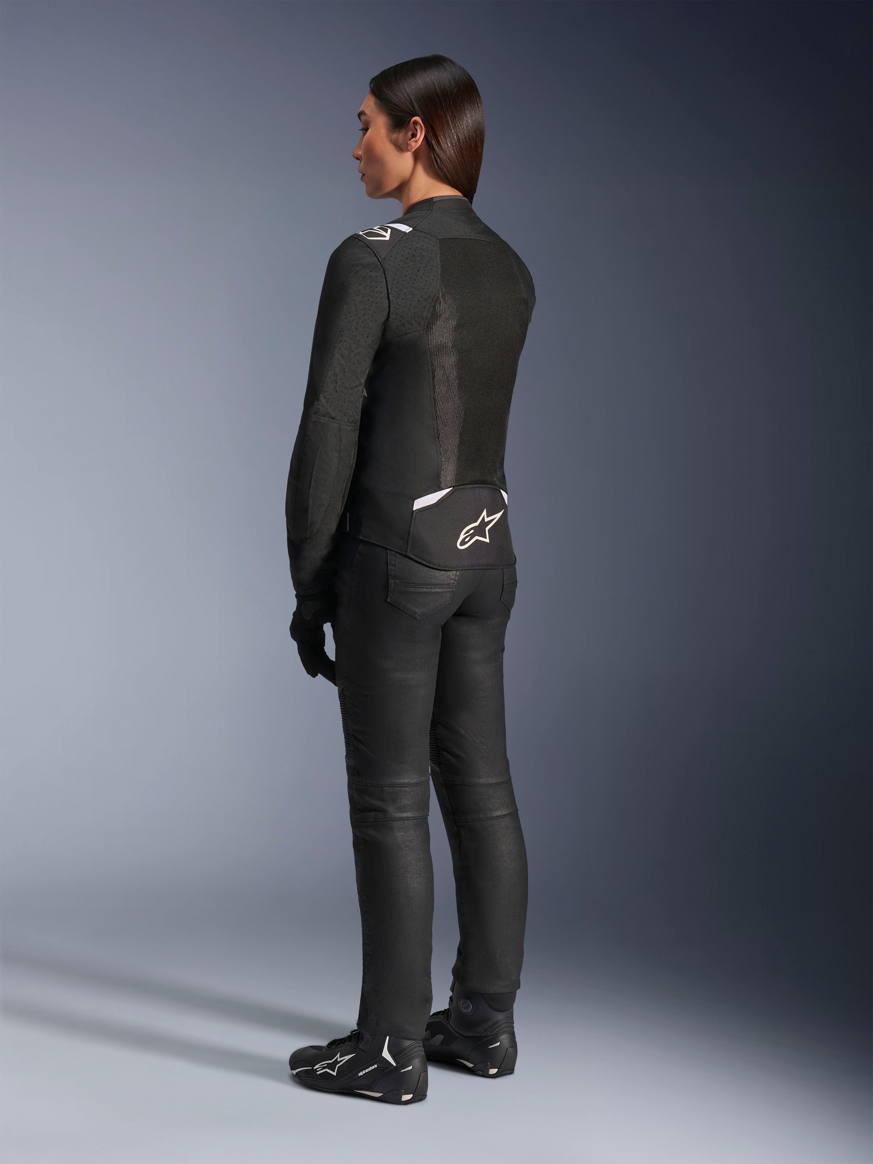 Alpinestars Stella T-SPS Air v2 Jacke, Schwarz und Weiß, Rückansicht mit Mesh-Einsätzen und Logo am unteren Rücken, kombiniert mit schwarzer Motorradhose und Motorradschuhen, sportliche Textil-Straßenausrüstung für Damen