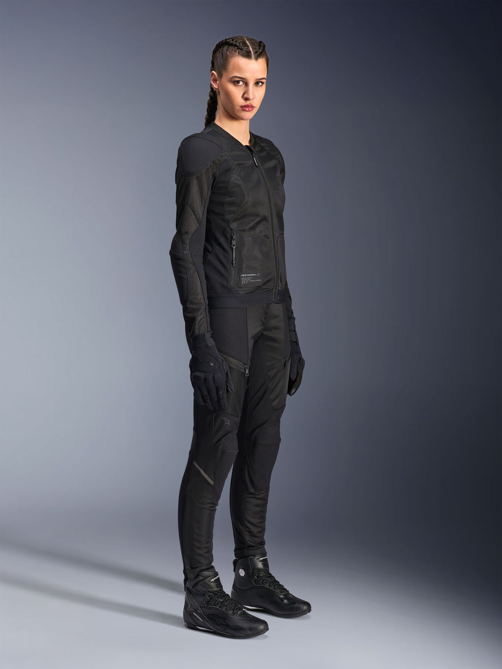 Motorradfahrerin in der Alpinestars Stella Troop-Air Jacke in Schwarz, mit technischer 2D-Mesh-Konstruktion, kombiniert mit passender schwarzer Motorradhose, Handschuhen und Stiefeln, gestylt für urbane Fahrten