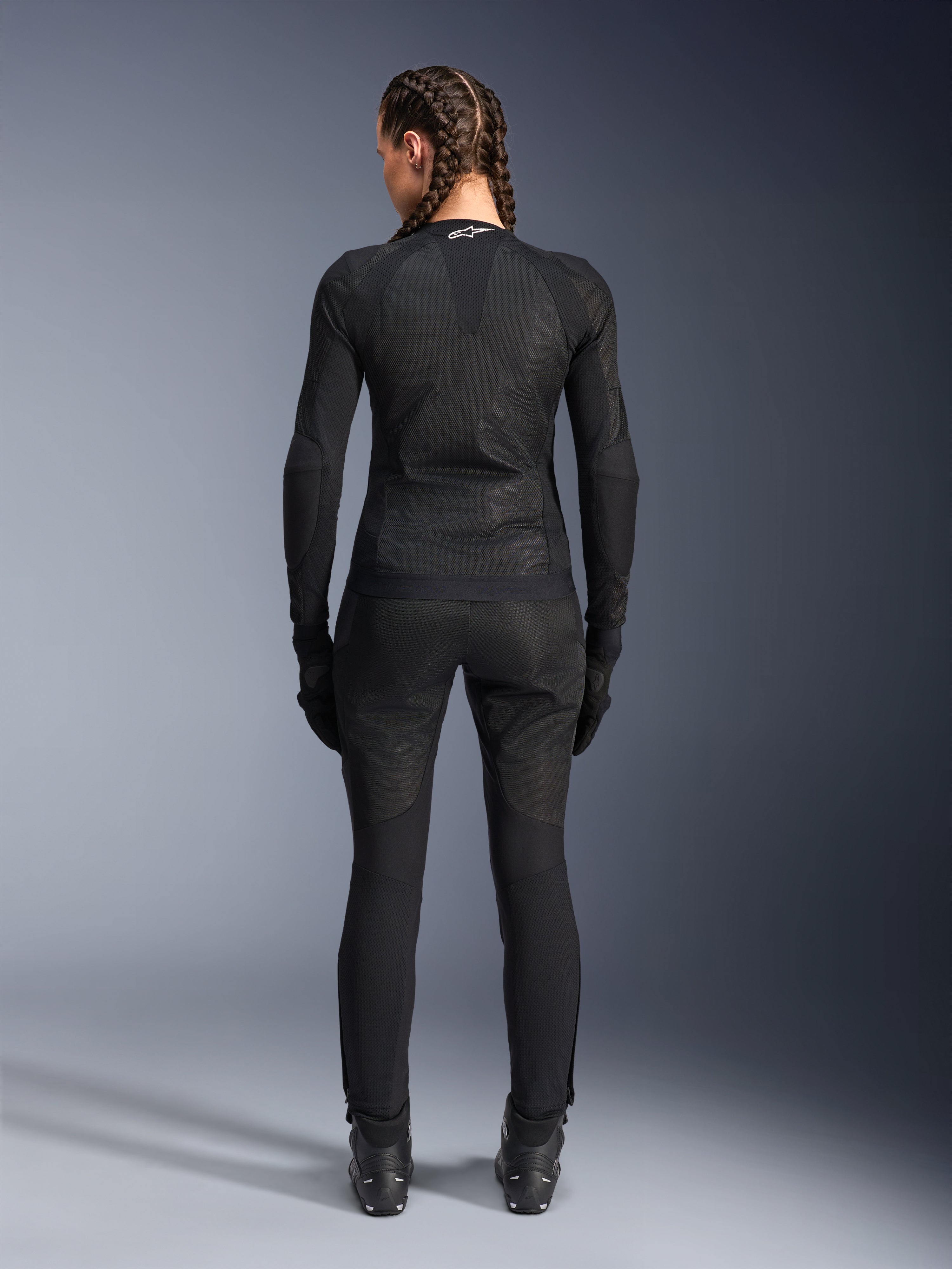 Alpinestars Stella Troop-Air Jacke, Damen-Motorradjacke, Schwarz, Rückansicht einer Fahrerin in technischer Mesh-Jacke, kombiniert mit passender schwarzer Motorradhose, Handschuhen und Stiefeln, schmal geschnittenes atmungsaktives Design mit weißem Alpinestars-Logo am Kragen