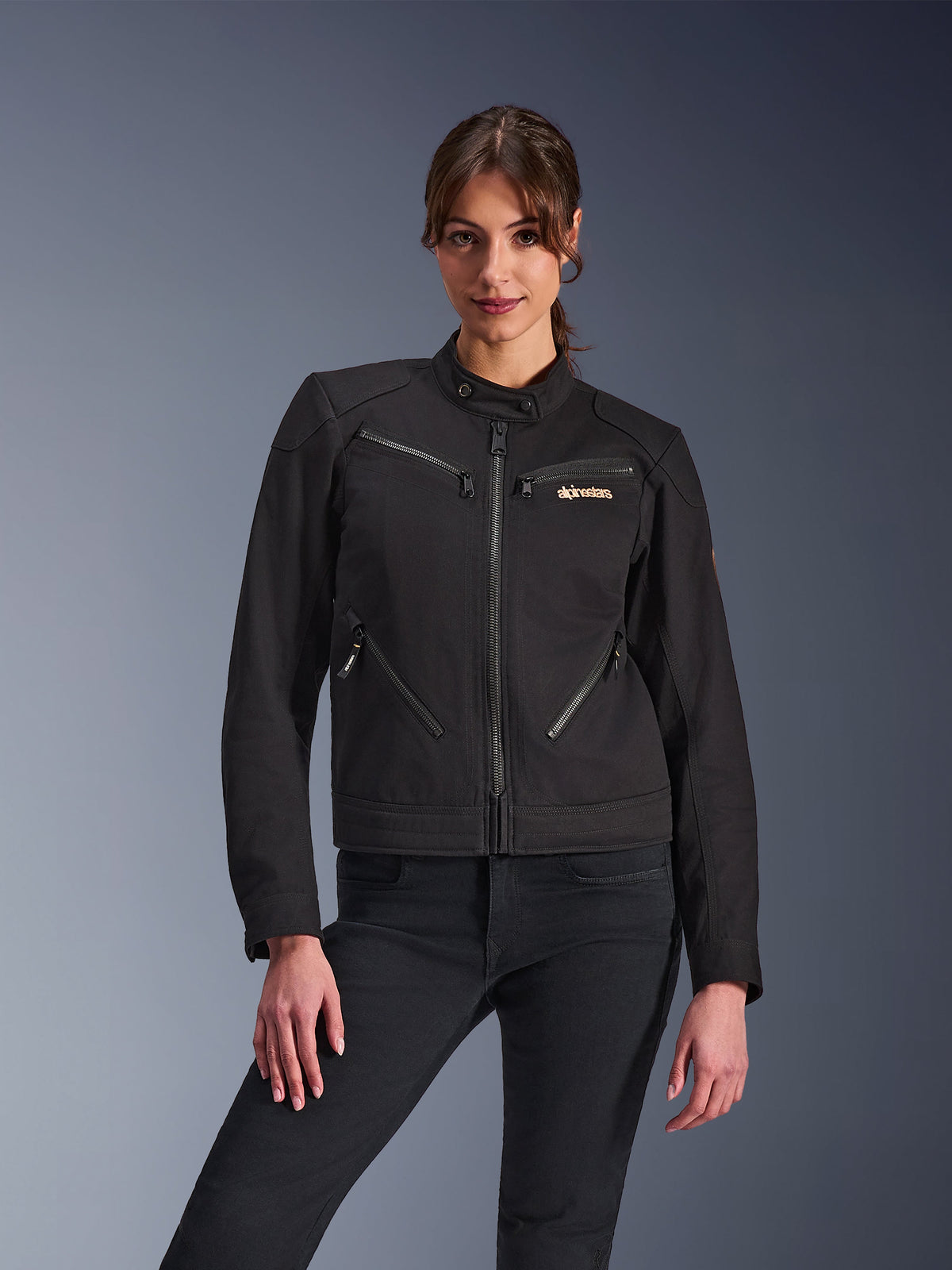 Alpinestars Stella Grace Damenjacke, Urbane Motorradjacke, Schwarz, Vorderansicht, mit mehreren Reißverschlusstaschen und einem Druckknopfkragen, kombiniert mit schwarzen Jeans, moderne Lifestyle-inspirierte Schutzausrüstung für Damen
