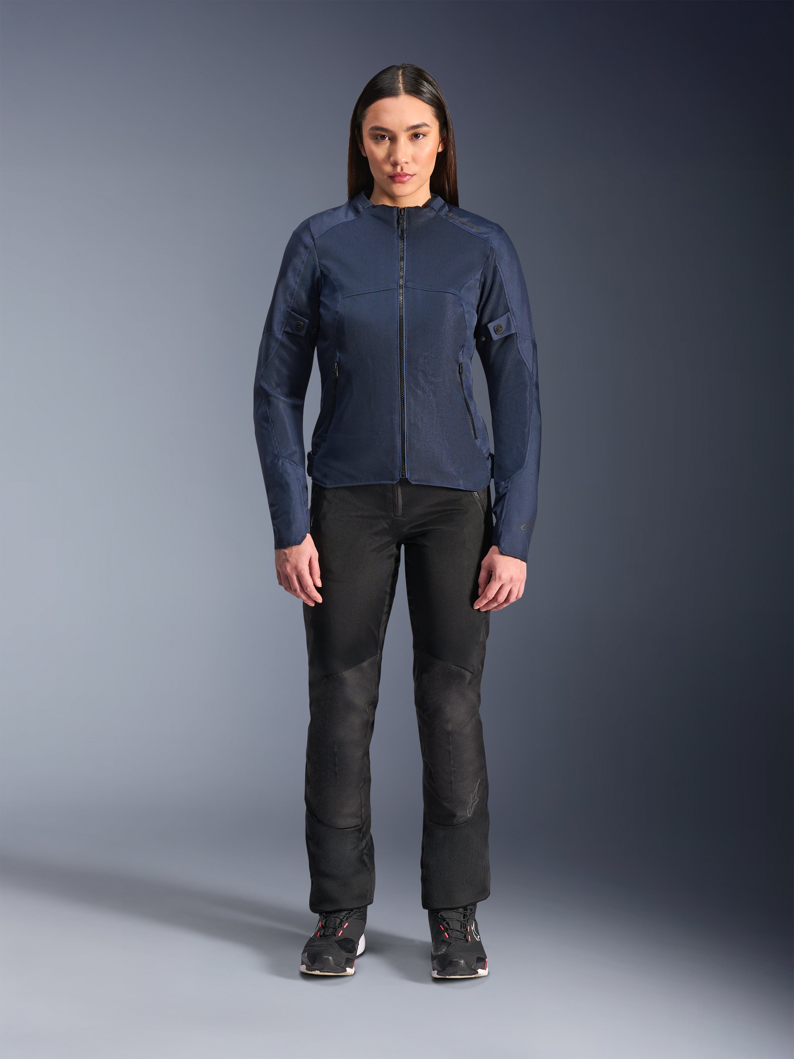 Weibliches Model trägt Alpinestars Stella C-1 Air Jacke in Blau, urbane Motorradjacke mit Tech-Mesh-Einsätzen, kombiniert mit schwarzer Motorradhose und schwarzen Sneakern, Studio-Frontansicht
