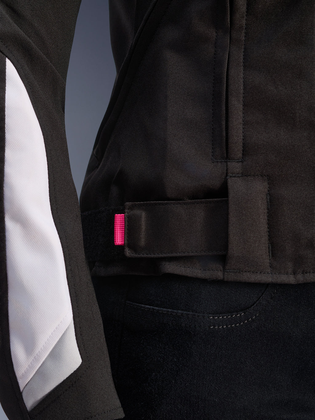 Alpinestars Stella T-GP Plus R V4 Jacke, Schwarz und Weiß, Nahaufnahme des verstellbaren Taillenriemens mit rosa Akzentlasche, strapazierfähige Textilkonstruktion mit weißen Ärmeleinsätzen, sportliche Damen-Motorradjacke