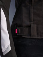 Alpinestars Stella T-GP Plus R V4 Jacke, Schwarz und Weiß, Nahaufnahme des verstellbaren Taillenriemens mit rosa Akzentlasche, strapazierfähige Textilkonstruktion mit weißen Ärmeleinsätzen, sportliche Damen-Motorradjacke