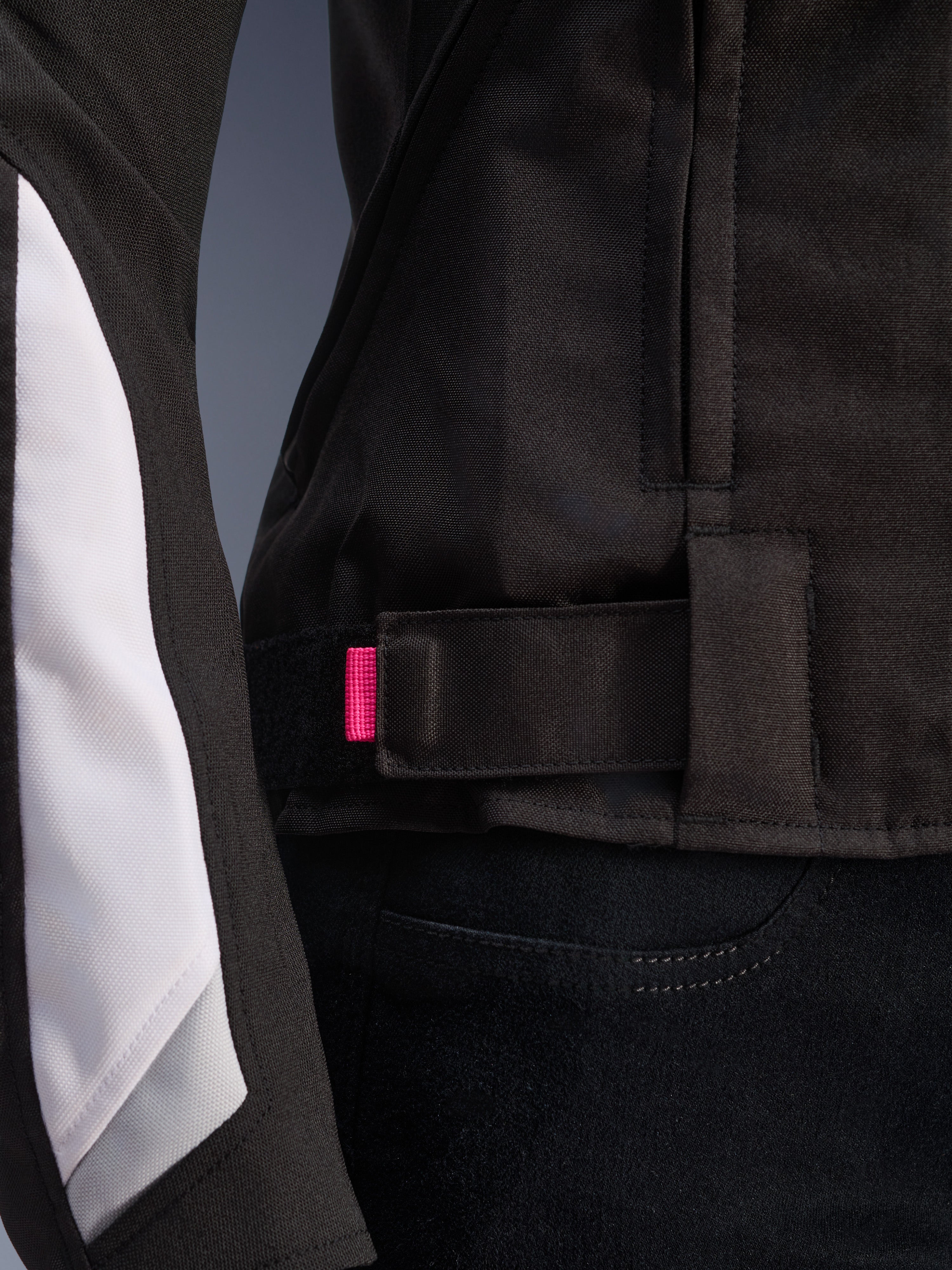 Alpinestars Stella T-GP Plus R V4 Jacke, Schwarz und Weiß, Nahaufnahme des verstellbaren Taillenriemens mit rosa Akzentlasche, strapazierfähige Textilkonstruktion mit weißen Ärmeleinsätzen, sportliche Damen-Motorradjacke