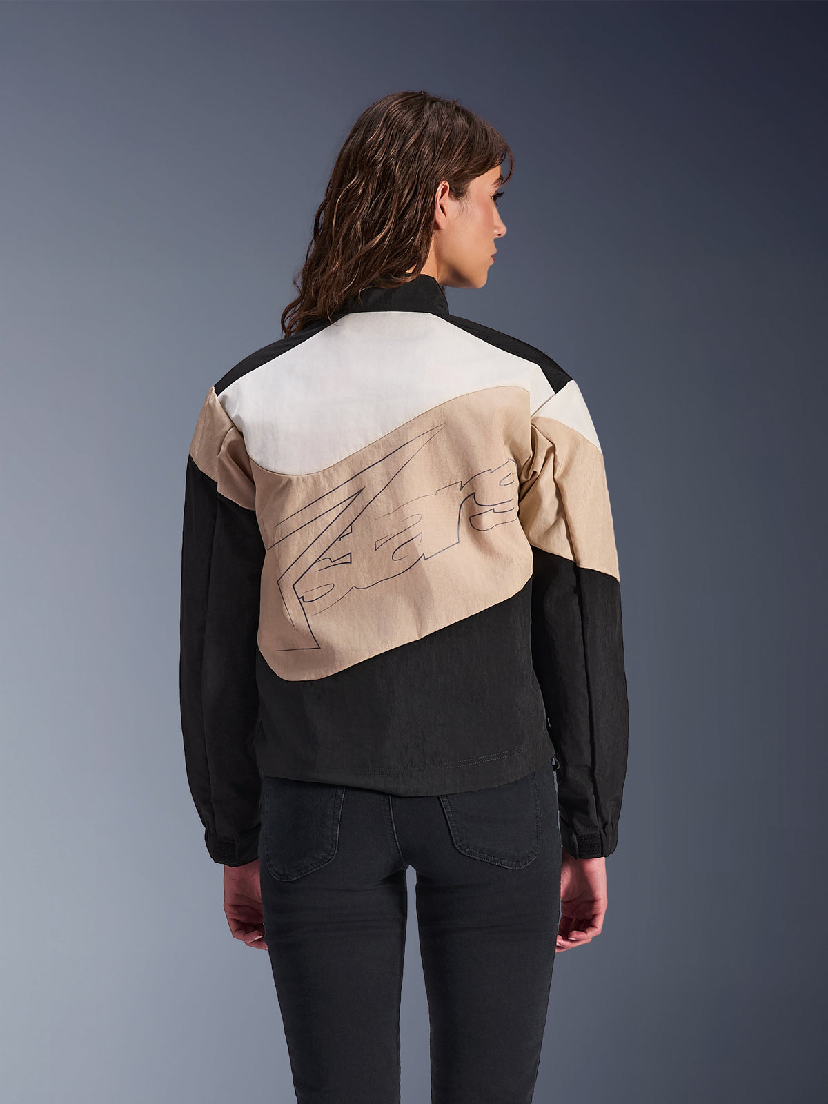 Alpinestars Stella Moshell Jacke, urbane Damen-Motorradjacke, Black Sand und Off-White, Rückansicht an einem Model, asymmetrisches Color-Block-Design mit großer Grafik auf dem Rücken, moderne Streetwear-inspirierte Schutzausrüstung
