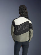 Frau von hinten in der Alpinestars Stella Moshell Jacke, urbane Motorradjacke in Schwarz, Grau und Off-White, mit großem weiß umrandetem Logo auf dem Rücken, kombiniert mit schwarzer Hose, moderne von Streetwear inspirierte Motorradausrüstung.
