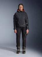 Weibliches Model in der Alpinestars Molly Air Jacke in Schwarz und Fluo Coral, Utility-inspiriertes Design mit Kapuze und korallenfarbenem Innenfutter, kombiniert mit schwarzer Motorradhose und Stiefeln, urbane zeitgenössische Motorradausrüstung