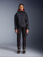 Alpinestars Actea Damenhose, schwarze Motorradhose für Damen mit roten Schriftelementen und Cargotaschen, getragen von einer Fahrerin mit schwarzer Kapuzenjacke, moderne urbane Motorradbekleidung