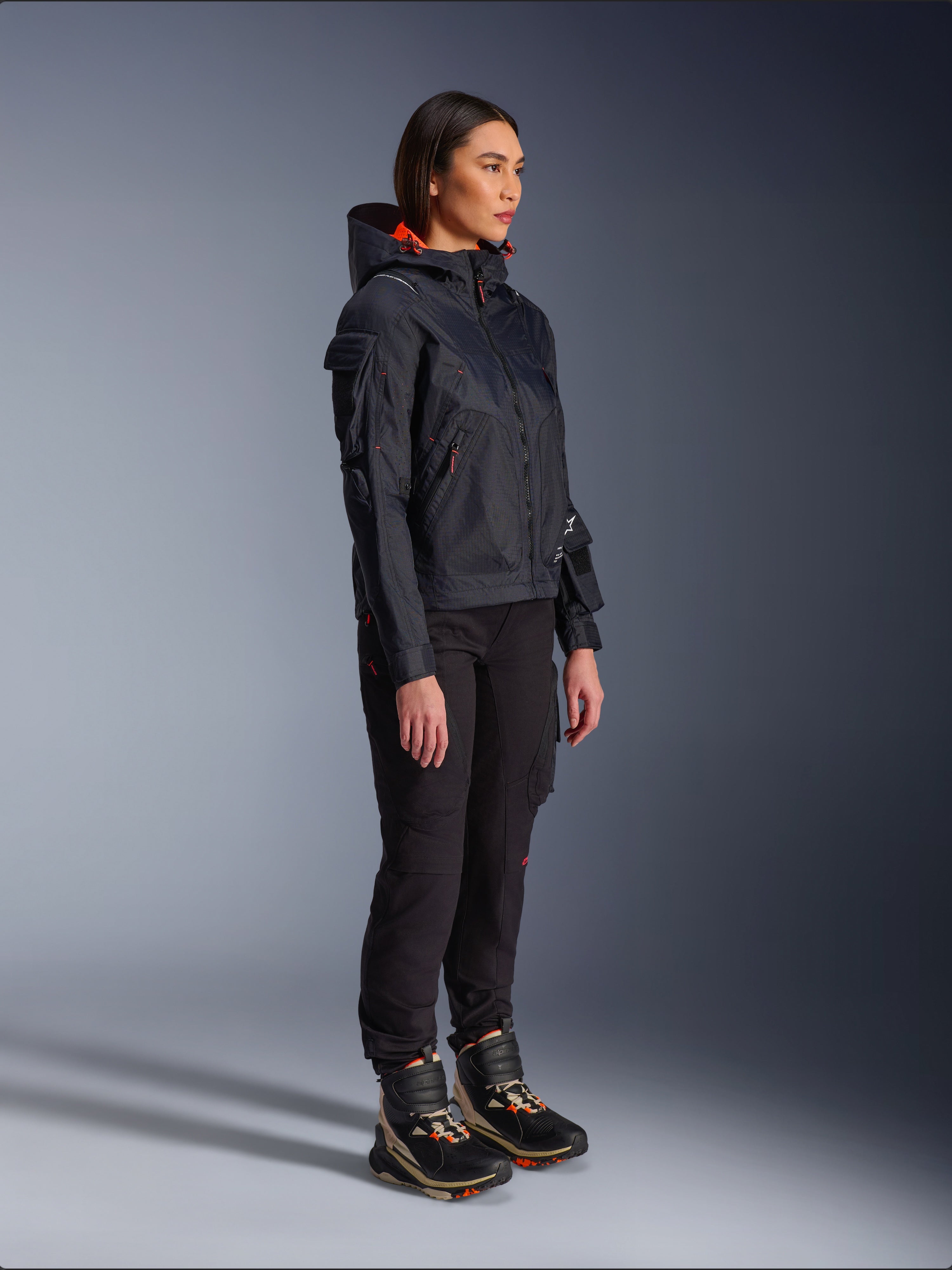 Alpinestars Actea Damen-Hose in Schwarz, reguläre Passform mit Cargotaschen, kombiniert mit einer schwarzen Molly Air Jacke mit orangefarbenen Akzenten und High-Top-Motorradschuhen, moderne urbane Motorradbekleidung für Damen
