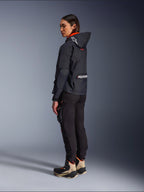 Motorradfahrerin in der Alpinestars Molly Air Jacke in Black Fluo Coral, Seitenansicht von hinten zeigt die Kapuze mit Astars-Logo und großem Alpinestars-Branding auf dem Rücken, kombiniert mit schwarzer Cargo-Motorradhose und sandfarbenen sowie schwarzen Adventure-Stiefeln, moderne urbane Motorradausrüstung für Damen