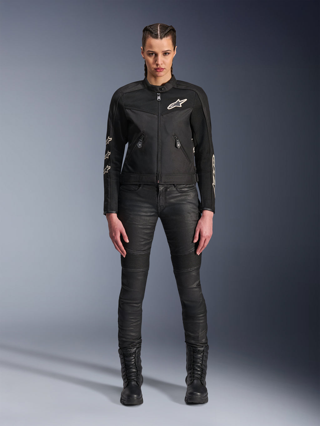 Weibliches Model trägt die Alpinestars Stella T-Dyno Air Jacke, Damen-Motorradjacke in Schwarz, mit 3D-Mesh-Einsätzen und weißen Astars-Logos, kombiniert mit einer schwarzen Slim-Fit-Fahrhose und schwarzen Schnürstiefeln, urbaner Motorrad-Stil.