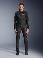 Weibliches Model trägt die Alpinestars Stella T-Dyno Air Jacke, Damen-Motorradjacke in Schwarz, mit 3D-Mesh-Einsätzen und weißen Astars-Logos, kombiniert mit einer schwarzen Slim-Fit-Fahrhose und schwarzen Schnürstiefeln, urbaner Motorrad-Stil.