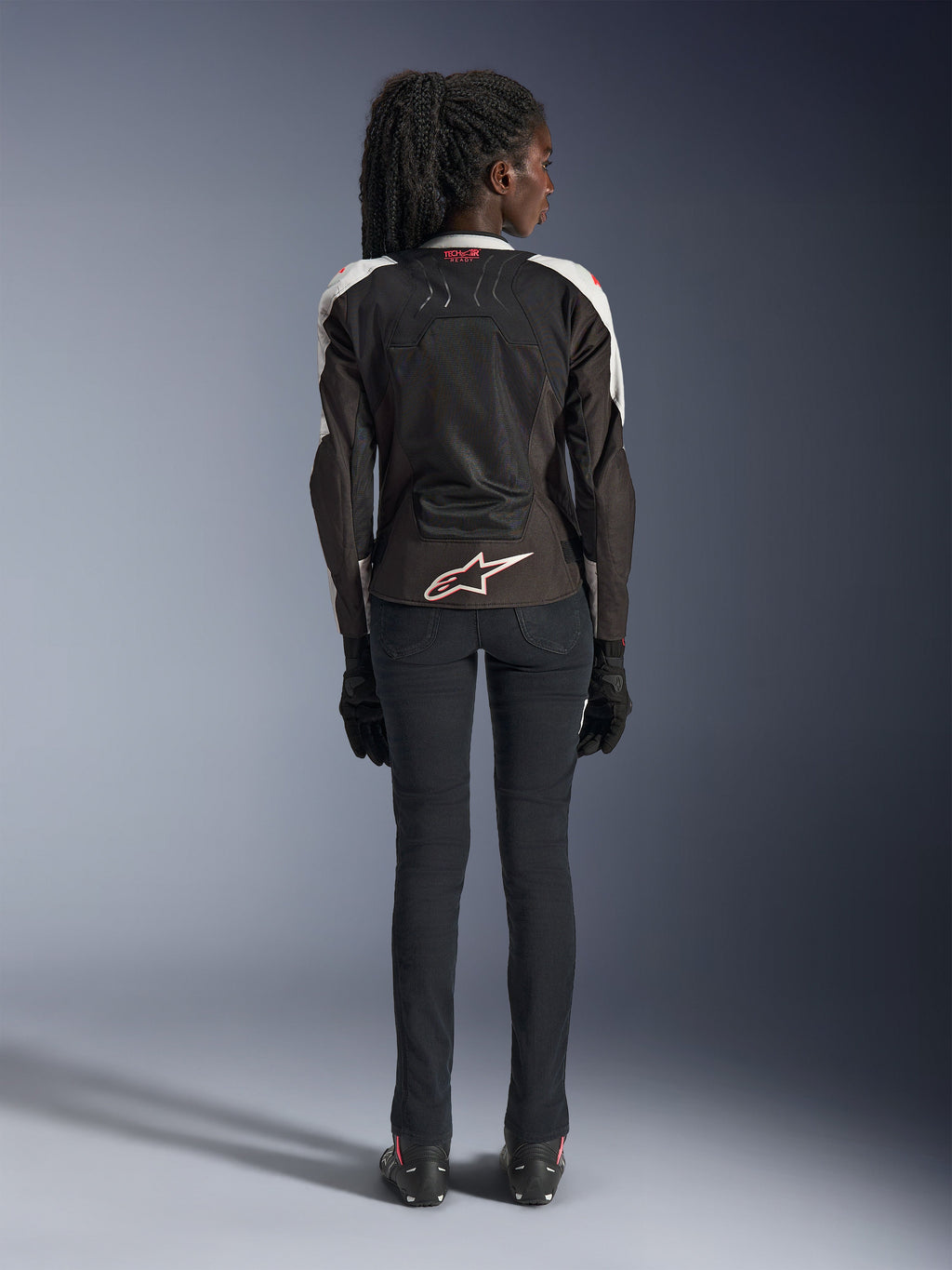 Alpinestars Stella SMX Air Damenjacke, Ice Gray Black Coral Fluo, Rückansicht mit belüfteten Mesh-Einsätzen, weißes Alpinestars-Logo am unteren Rücken und Tech-Air Ready Branding am Kragen, kombiniert mit schwarzer Motorradhose und Handschuhen.