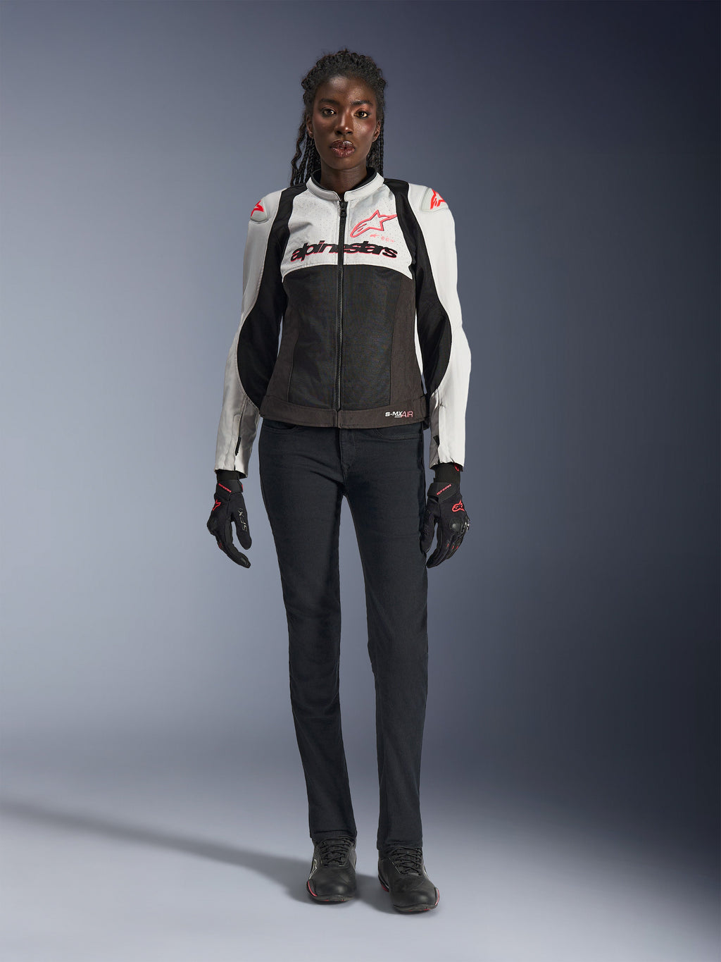 Alpinestars Stella SMX Air Jacke, Ice Gray, Schwarz und Coral Fluo, getragen von einem weiblichen Model mit schwarzer Motorradhose und Handschuhen, mit Mesh-Chassis und schützenden Schulter-Slidern, sportliche Motorradausrüstung für Damen