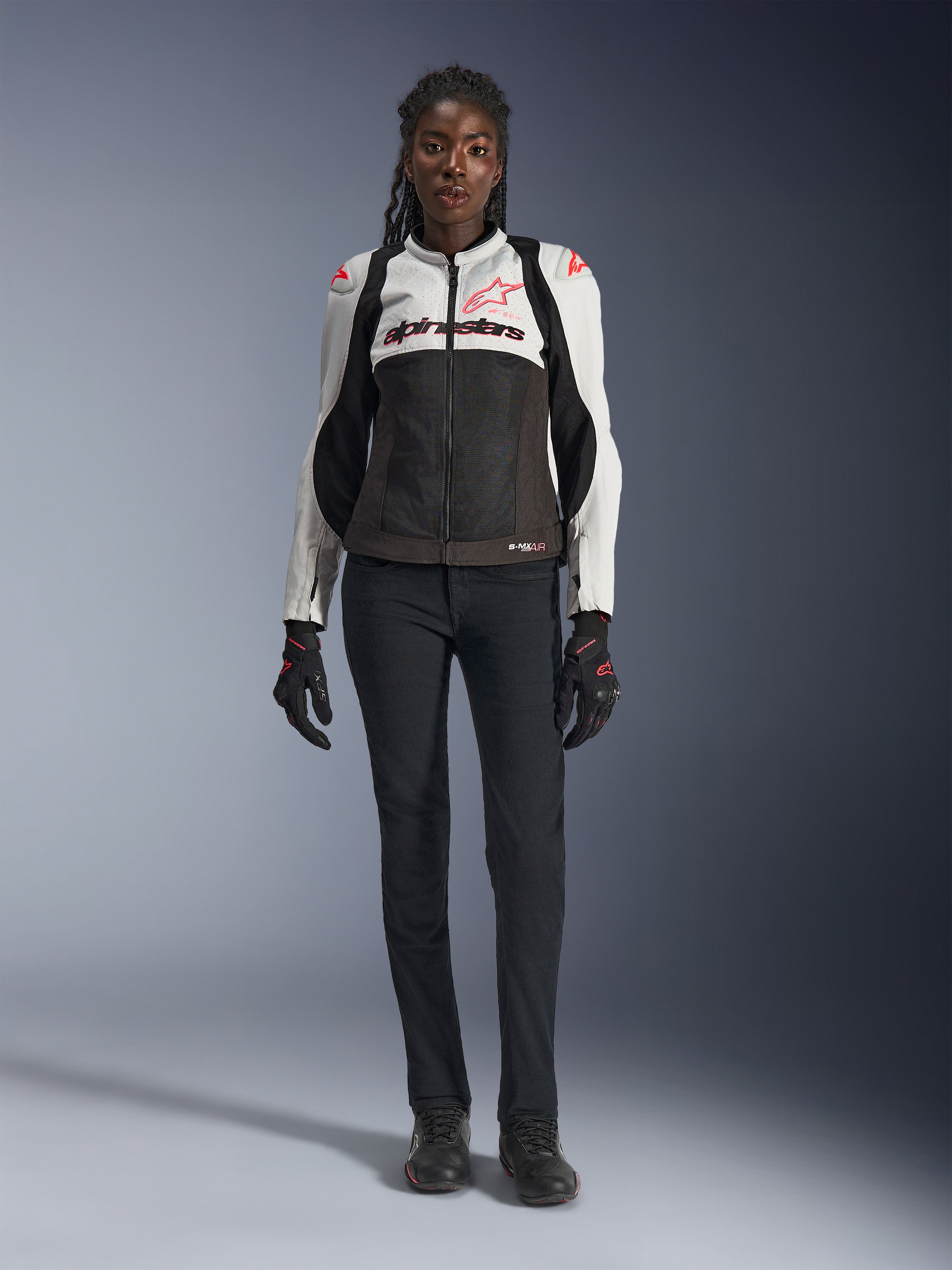 Alpinestars Stella SMX Air Jacke, Ice Gray, Schwarz und Coral Fluo, getragen von einem weiblichen Model mit schwarzer Motorradhose und Handschuhen, mit Mesh-Chassis und schützenden Schulter-Slidern, sportliche Motorradausrüstung für Damen