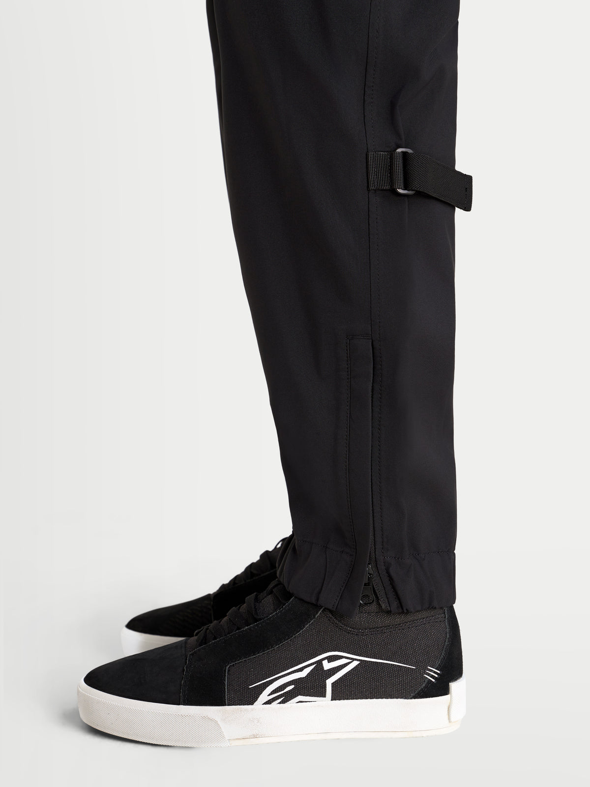 Alpinestars Juggernaut V 2 Drystar Hose, urbane Motorradhose in Schwarz, Nahaufnahme der Seitenansicht mit Unterschenkelverstellung und elastischem Saum mit Reißverschlussöffnung