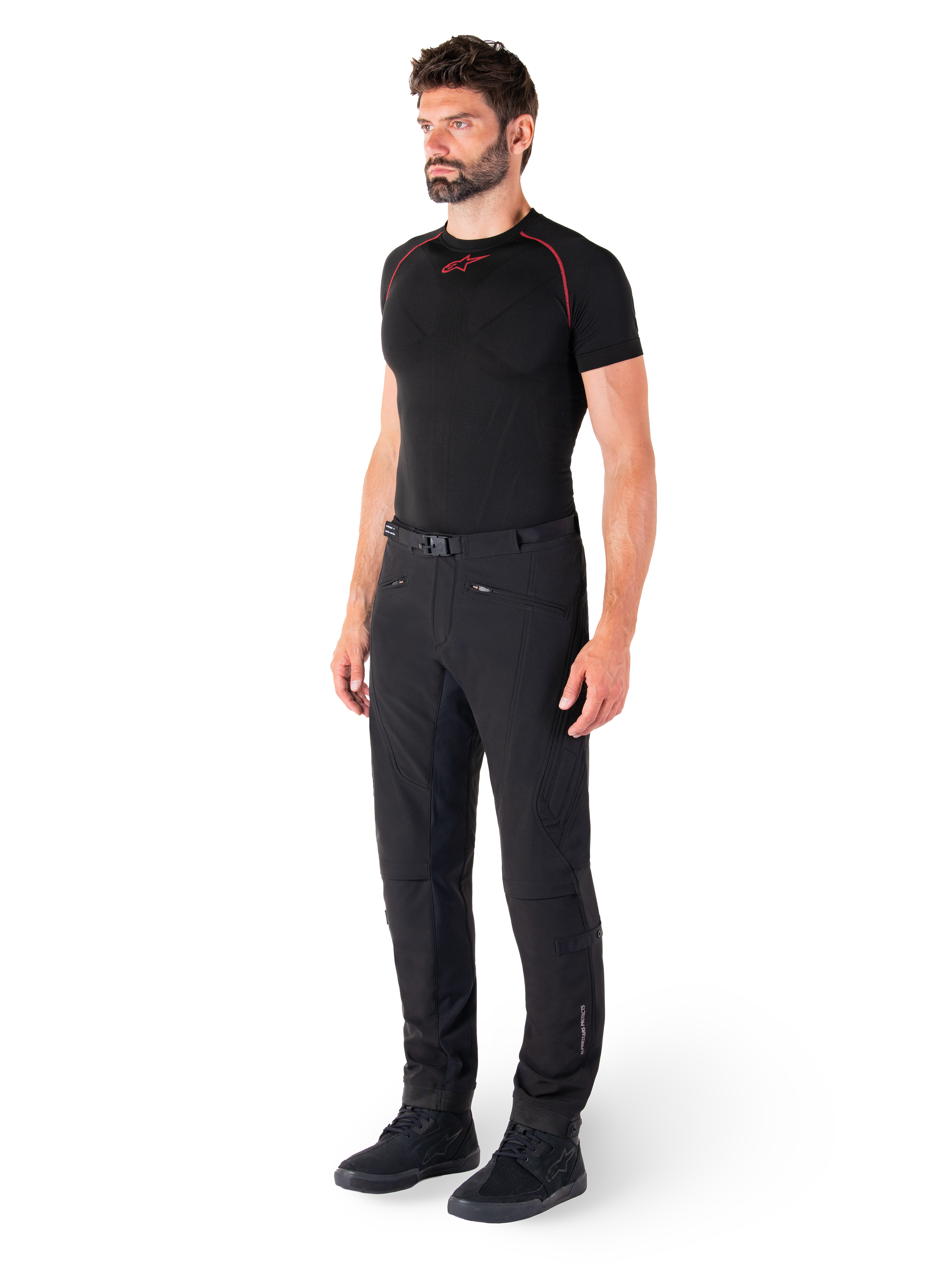 Alpinestars Alden Hose, Urbane Motorradhose, Schwarz, Softshell-Textil in regulärer Passform, getragen von einem Model mit schwarzem Base-Layer und Motorradschuhen, mit Taillengürtel mit Magnetverschluss und Reißverschlusstaschen.