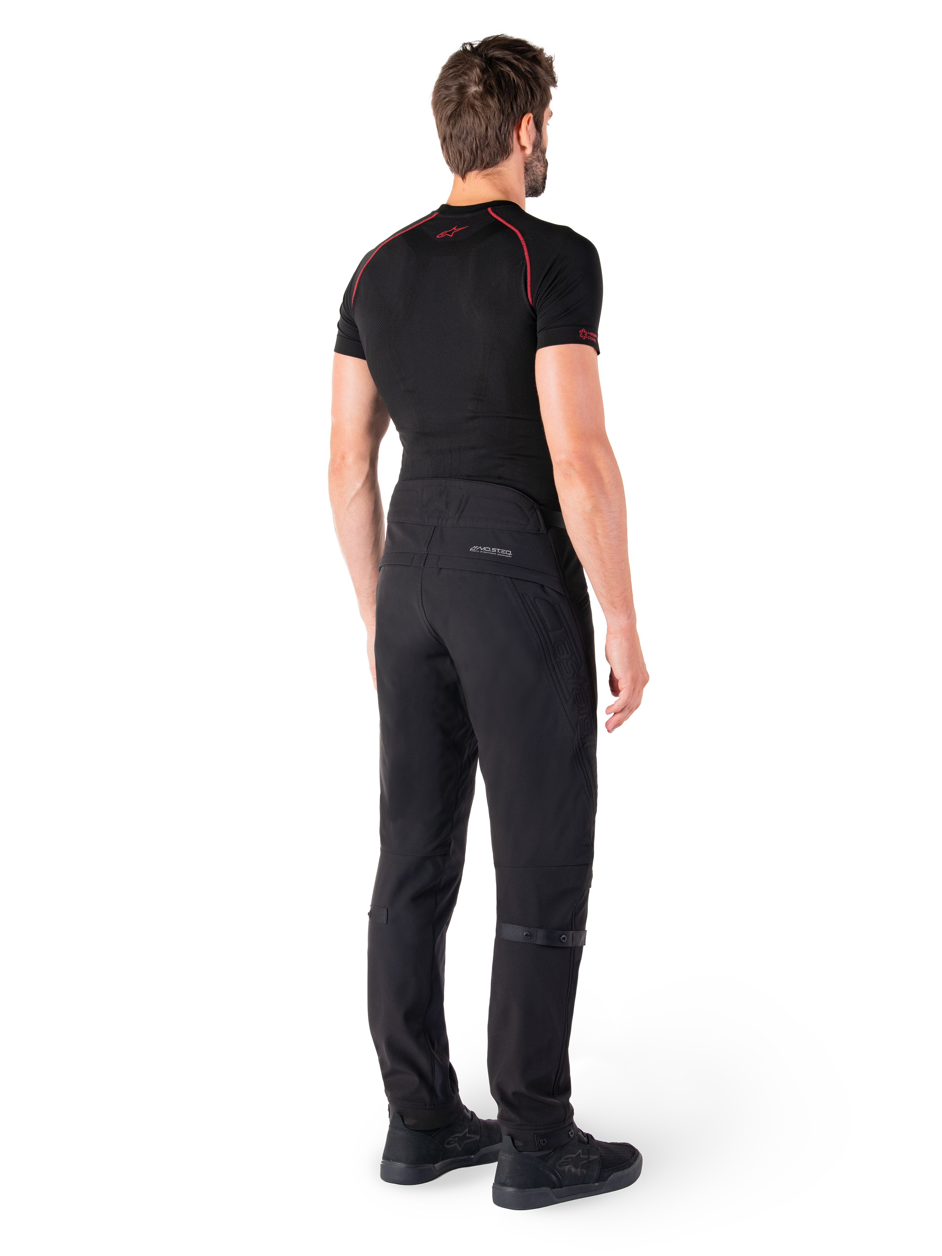 Alpinestars Alden Hose, Schwarz, urbane Motorradhose von hinten an einem Model gezeigt, getragen mit einem schwarzen kurzärmeligen Baselayer und schwarzen Motorradschuhen, mit gesteppten Details und reflektierendem MO.ST.EQ. Branding auf der Rückenpasse.