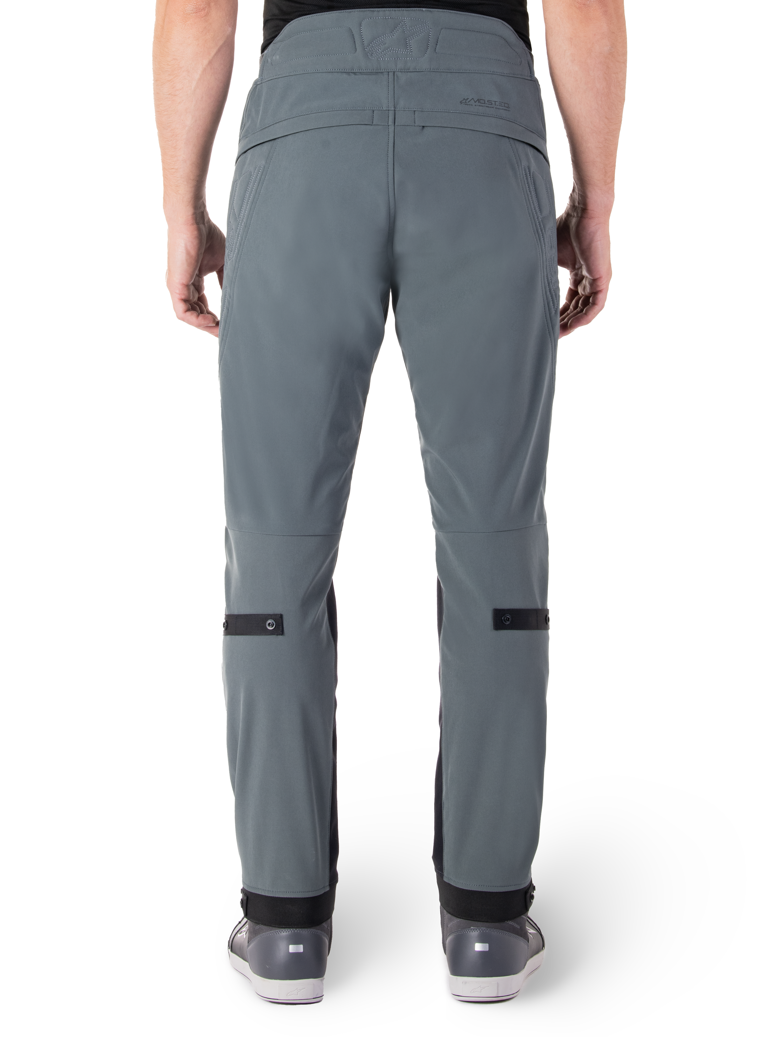 Alpinestars Alden Hose, Urban Gray, Rückansicht einer urbanen Motorradhose für Herren, schmale Passform unterhalb des Knies mit schwarzen Wadenverstellriemen, hoher Bund mit MO.ST.EQ. Wortmarke auf der Rückenpasse, getragen mit grauen Reitschuhen
