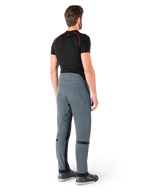 Alpinestars Alden Hose, Urban Grau, Rückansicht, technische Textil-Motorradhose mit gesteppten Details am oberen hinteren Bund und an den Beinen, kombiniert mit einem schwarzen Baselayer und grauen Motorradschuhen, moderner urbaner Streetwear-Stil.
