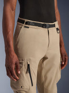 Alpinestars Flex-AST Cargo Hose - Short, Hellbeige, Nahaufnahme von Taille und Oberschenkel, mit schwarzem verstellbarem Gürtel mit Alpinestars-Branding, Metall-D-Ring und funktionalen Cargotaschen mit Reißverschlüssen und Druckknopfklappen, moderne urbane Motorradausrüstung