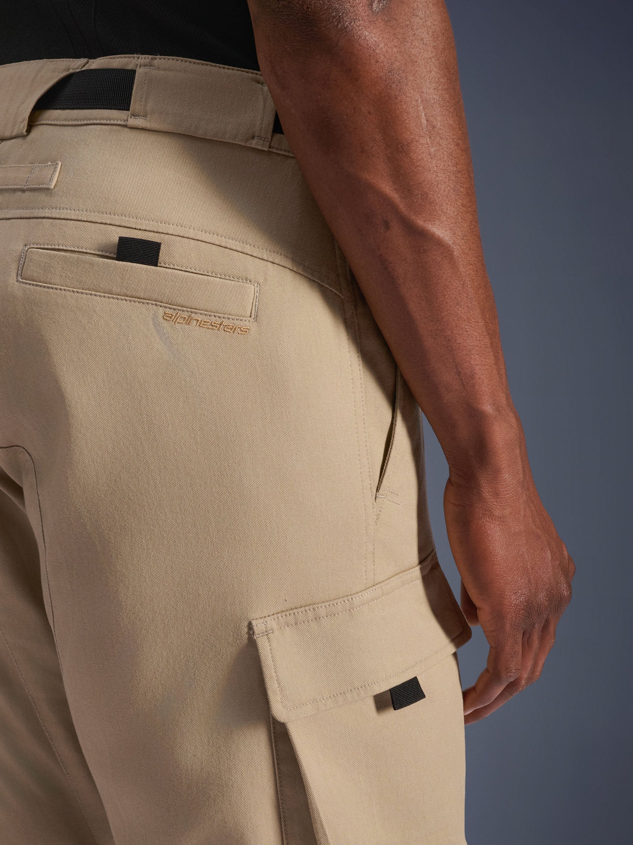 Alpinestars Flex-AST Cargo Pants, Light Beige, close-up of hip and side cargo pockets, featuring embroidered brand logo, black pull tabs, and military-inspired twill design for urban motorcycle riders