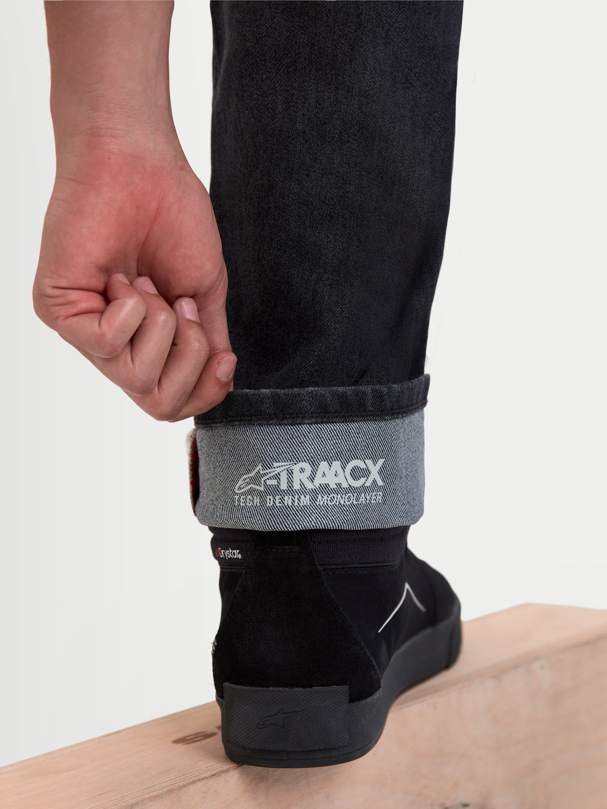 Alpinestars Flex Ast 8 Denim Hose Short, urbane Motorrad-Denim-Hose in Schwarz, Detailansicht des umgeschlagenen Beinabschlusses mit A-TRAACX Tech Denim Monolayer-Branding und Motorradschuhen