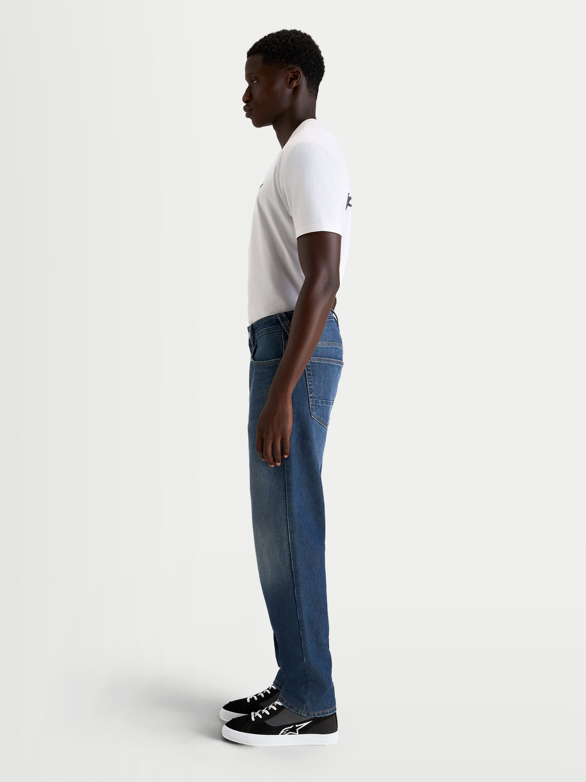 Alpinestars Flex Ast 8 Denim Hose, urbane Motorrad-Jeans für Herren in Mittelblau, Seitenprofil-Ansicht an einem Model mit weißem T-Shirt und lässigen Motorradschuhen, AA-zertifizierter, einlagiger Jeansstoff mit Stretch-Konstruktion