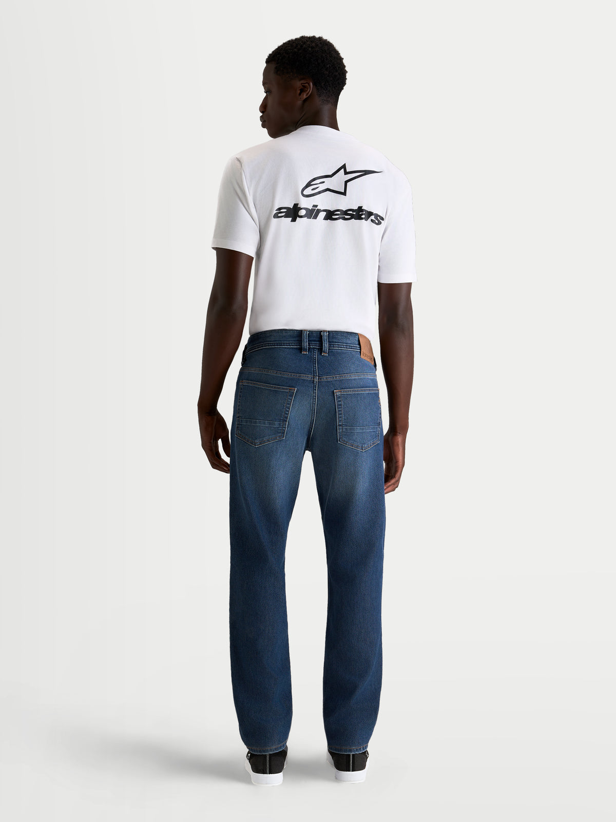 Alpinestars Flex Ast 8 Denim Hose, urbane Herren-Motorradjeans in Mittelblau, Rückansicht mit klassischem Fünf-Taschen-Design, getragen von einem Model mit weißem T-Shirt