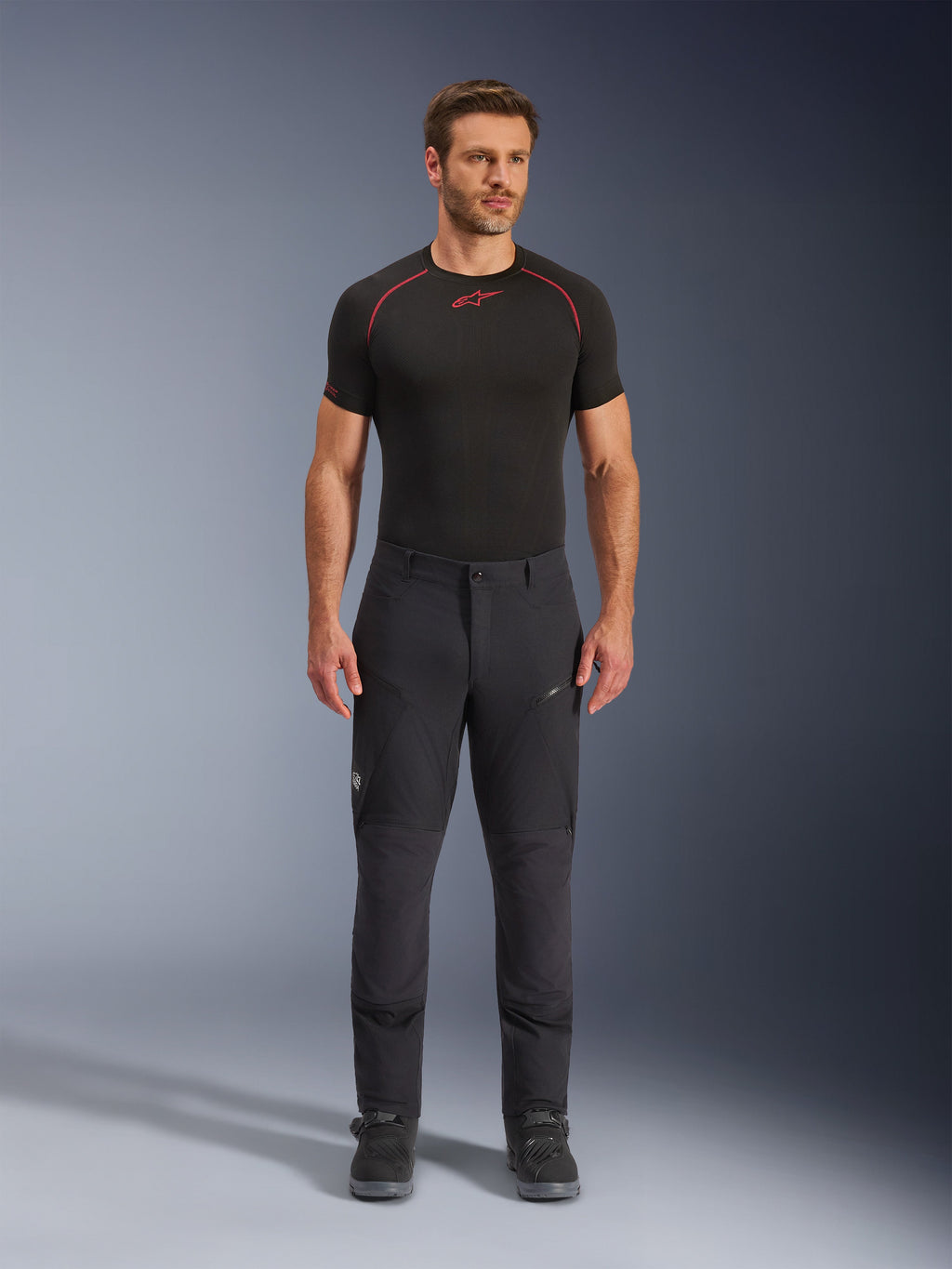 Alpinestars Flex-AST Explorer Hose, schwarze Adventure-Touring-Motorradhose, Mann in eng anliegender Textilhose mit Reißverschluss-Cargotaschen und verstärkten Einsätzen, kombiniert mit einem schwarzen Base-Layer und Motorradstiefeln, strapazierfähiger Schutz für Adventure-Fahrten