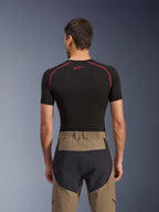 Alpinestars Flex-AST Explorer Pants, rear view on model, Walnut Black, featuring tan textile with reinforced black seat panels and an elasticated waistband, paired with a black short-sleeve base layer with red stitching.