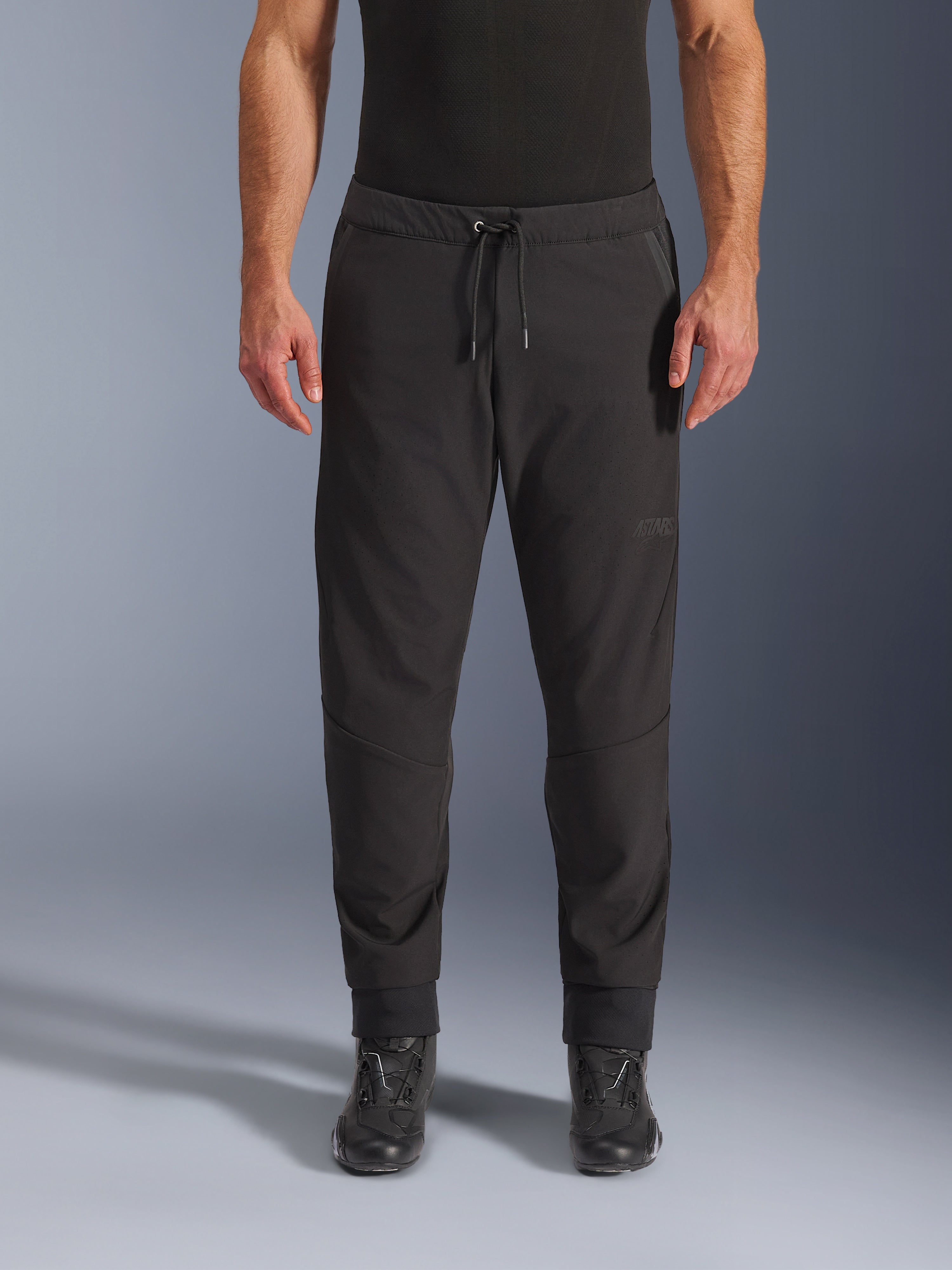 Alpinestars Aeroshell Airflow Pants, Black technical motorcycle pants, featuring a stretch softshell chassis with laser-perforated zones, drawstring waistband, and ASTARS logo, worn with black boots for sport and touring riders.