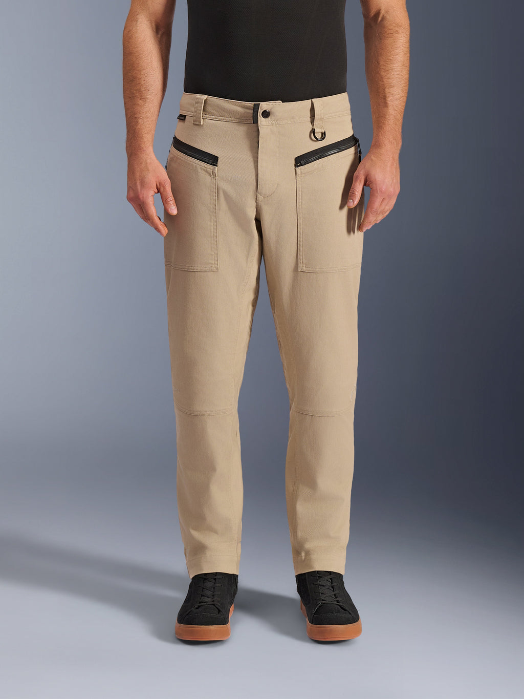 Alpinestars Flex-AST Canvas-Hose, urbane Motorradhose, Braun, Heritage-Workwear-Styling, mit schwarzen horizontalen Reißverschlusstaschen vorne und D-Ring an der Gürtelschlaufe, getragen mit schwarzem Shirt und Schuhen, Studioansicht von vorne