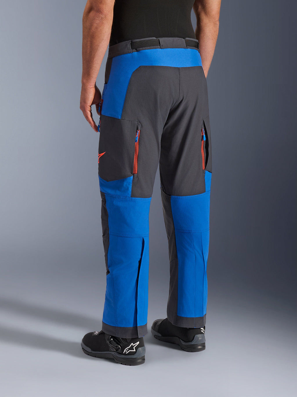 Alpinestars Maxdura Dual Hose, Königsblau und Dunkelgrau, Rückansicht mit Reißverschlusstaschen und Belüftungszonen, Überstiefel-Passform getragen mit schwarzen Alpinestars Stiefeln, strapazierfähige Adventure- und Dual-Sport-Ausrüstung