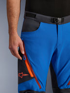 Alpinestars Maxdura Dual Hose in Royalblau und Dunkelgrau, Nahaufnahme des Hosenbundes mit Magnetverschluss, Cargotasche mit Reißverschluss, orangefarbenen Details und rotem Alpinestars-Logo, technische Adventure-Motorradausrüstung