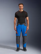 Alpinestars Maxdura Dual Hose, Adventure-Motorradhose, Royalblau und Dunkelgrau, orangefarbene Reißverschluss-Akzente, getragen mit einem schwarzen Alpinestars Base Layer und schwarzen Stiefeln, mit verstärkten Knieeinsätzen und technischem Offroad-Design