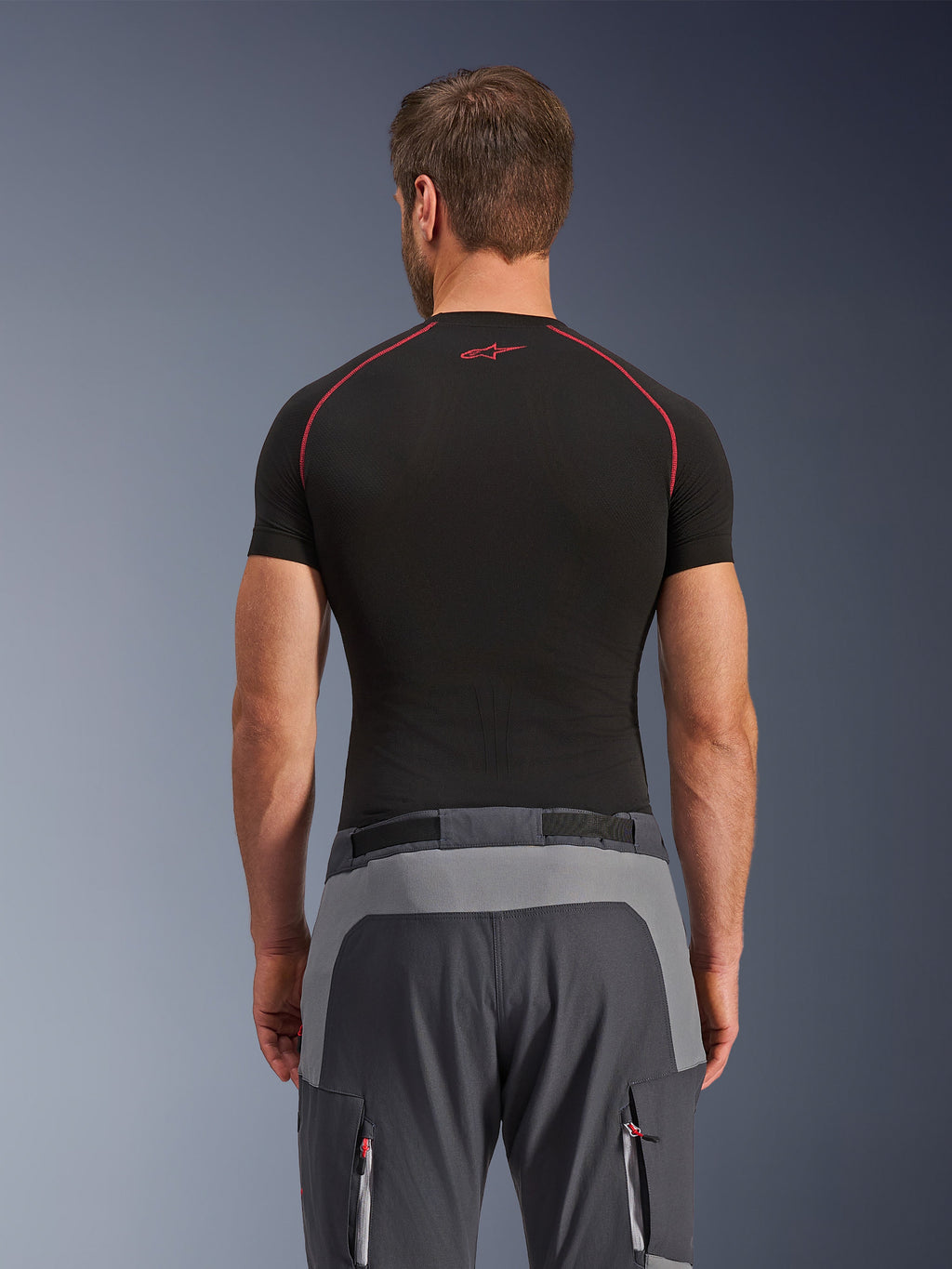 Alpinestars Maxdura Dual Hose, Adventure-Motorradhose, Dunkelgrau und Tiefgrau, Rückansicht mit verstärkten Paneelen an Gesäß und Taille, getragen mit schwarzem kurzärmeligem Baselayer, Reißverschlusstaschen mit roten Details