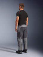Alpinestars Maxdura Dual Hose, Adventure-Motorradhose, Dunkelgrau und Tiefgrau, Rückansicht am Modell, rote Akzente an Reißverschlüssen und Logo, verstärkte graue Paneele, Cargotaschen und Over-Boot-Passform