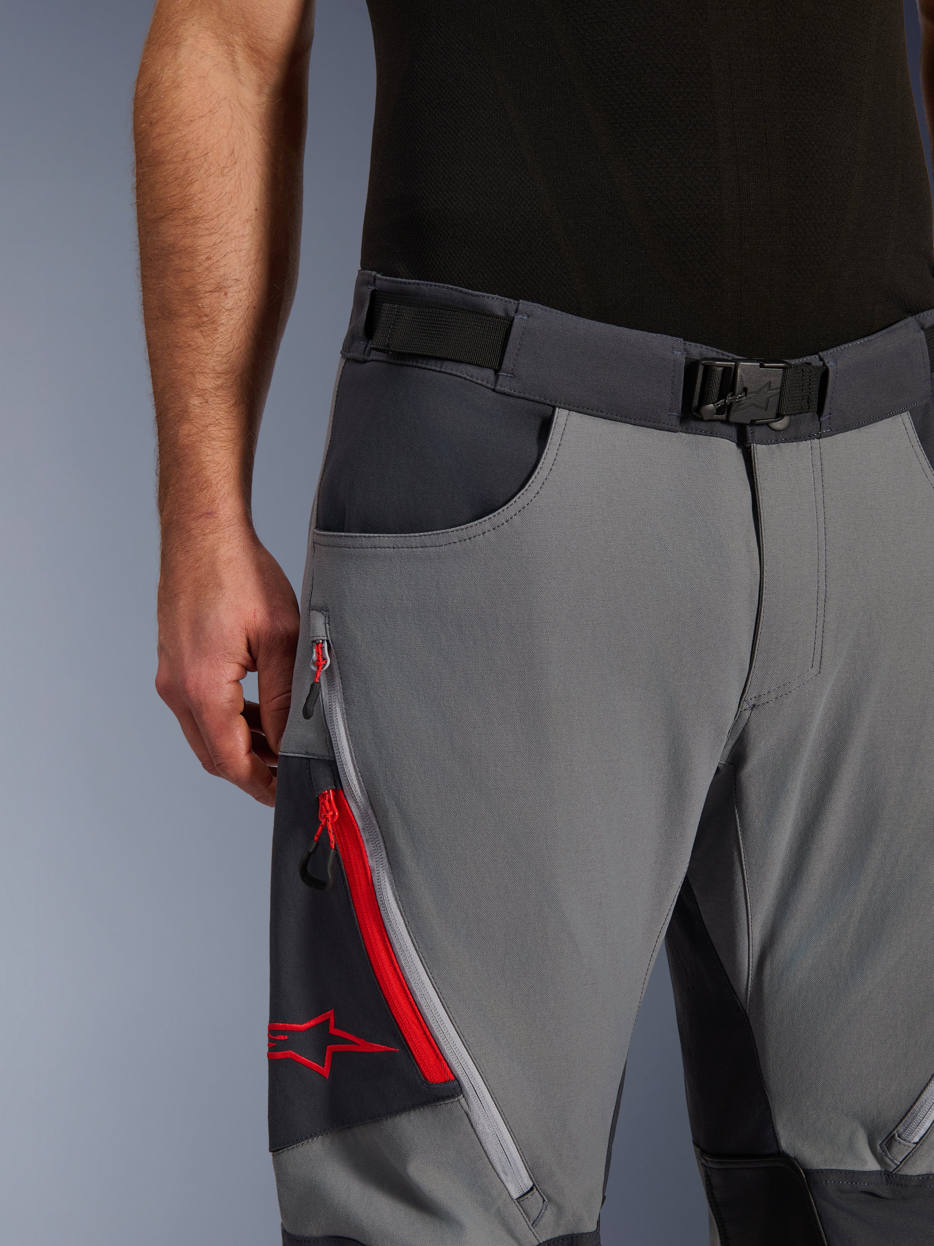 Alpinestars Maxdura Dual Hose, Adventure-Motorradhose, Dunkelgrau und Tiefgrau, Nahaufnahme mit verstellbarem Taillengürtel mit Magnetschnalle, Cargotasche mit Reißverschluss, roten Details und Alpinestars-Logo.