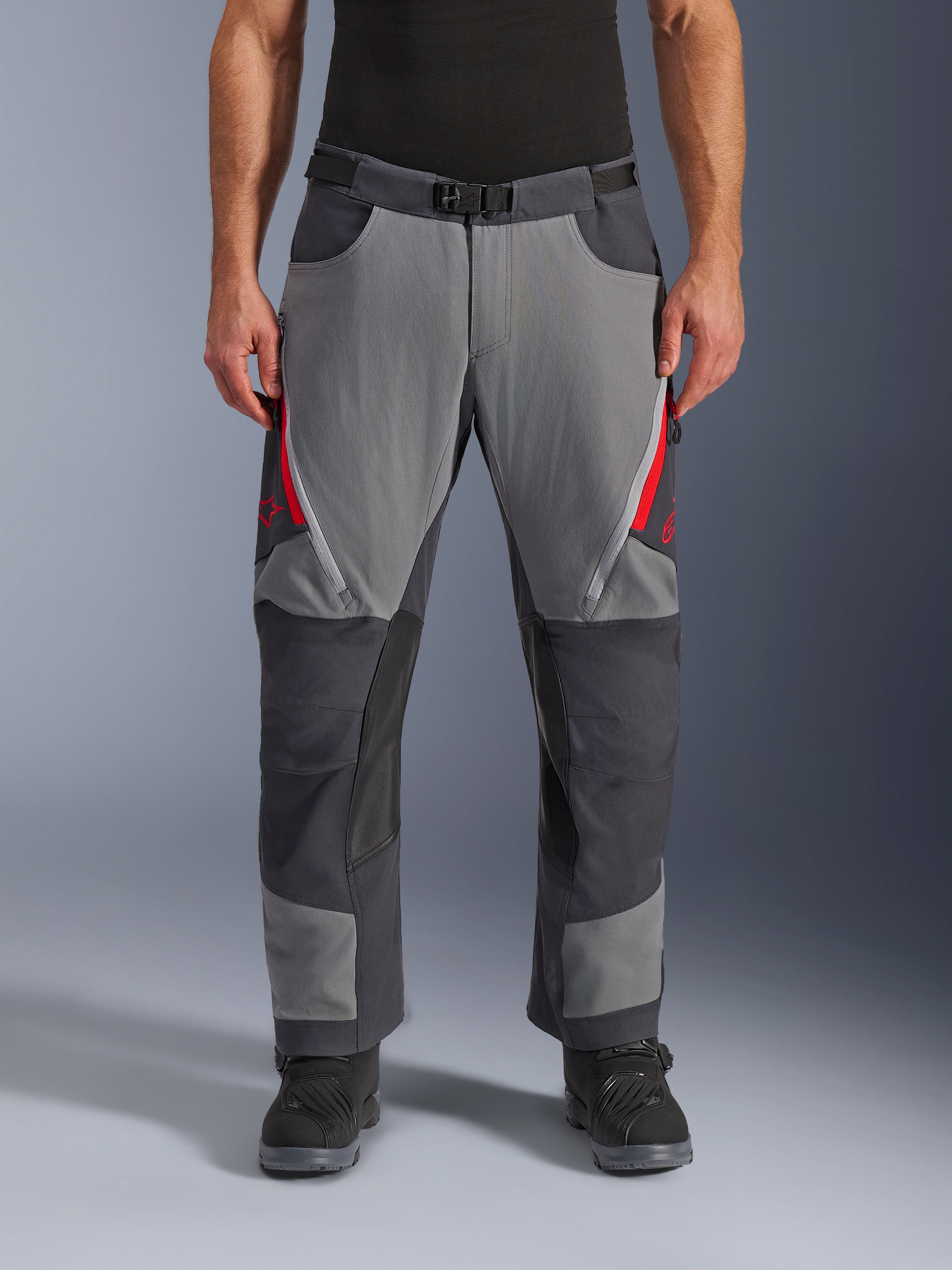 Alpinestars Maxdura Dual Hose, Adventure-Motorradhose, Dunkelgrau und Tiefgrau mit roten Akzenten, Vorderansicht mit Reißverschluss-Belüftungsöffnungen an den Oberschenkeln, Gürtel mit Magnetschnalle und verstärkten Kniepaneelen, Over-Boot-Design für Dual-Sport-Fahrten.