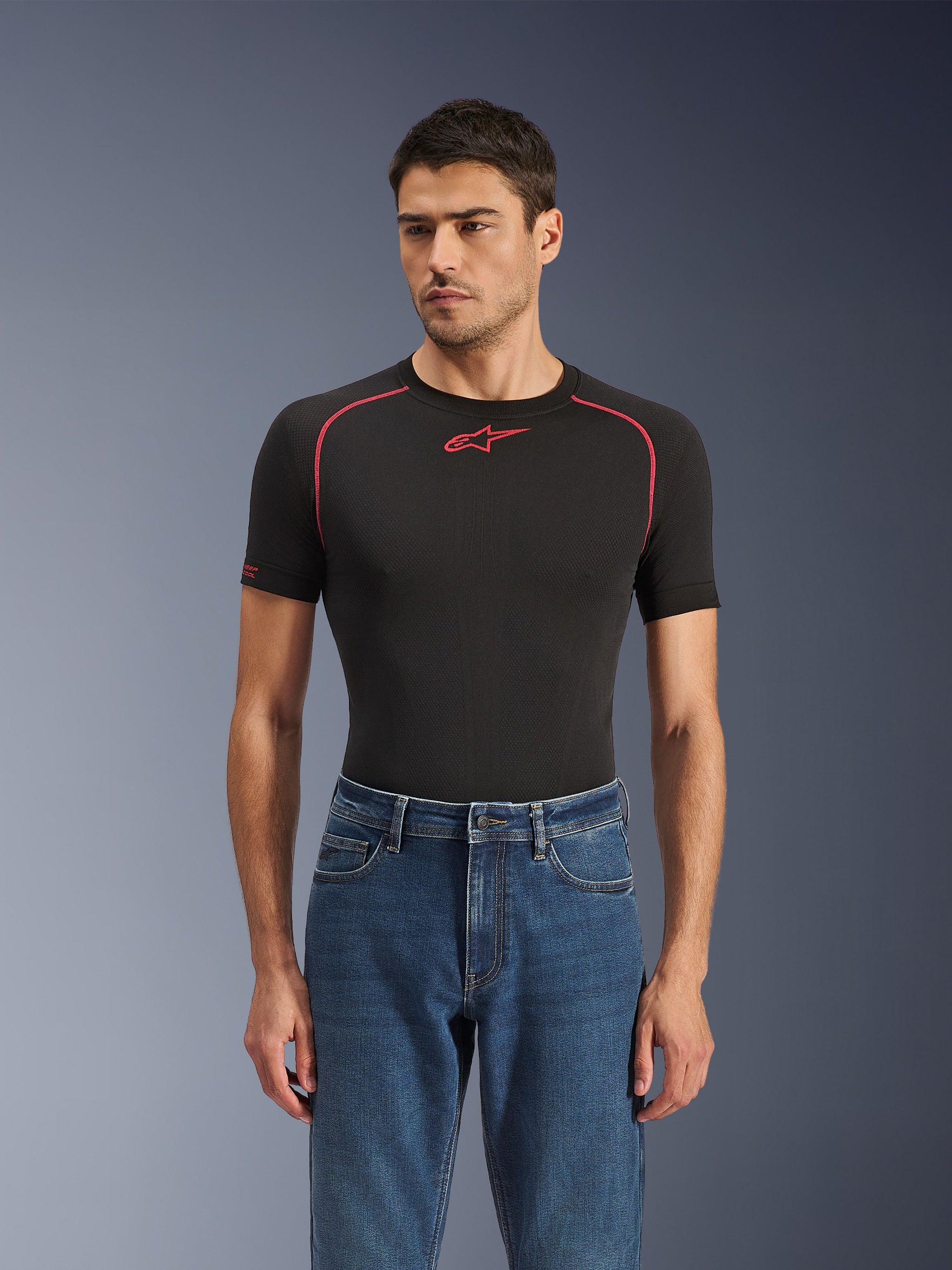 Alpinestars Flex-AST 5 Denim Hose in Indigo Washed, urbane Motorradjeans mit konischer Passform, getragen von einem männlichen Model mit schwarzem, kurzärmeligem Base Layer mit roten Akzenten, lässiges Road-to-Street-Styling