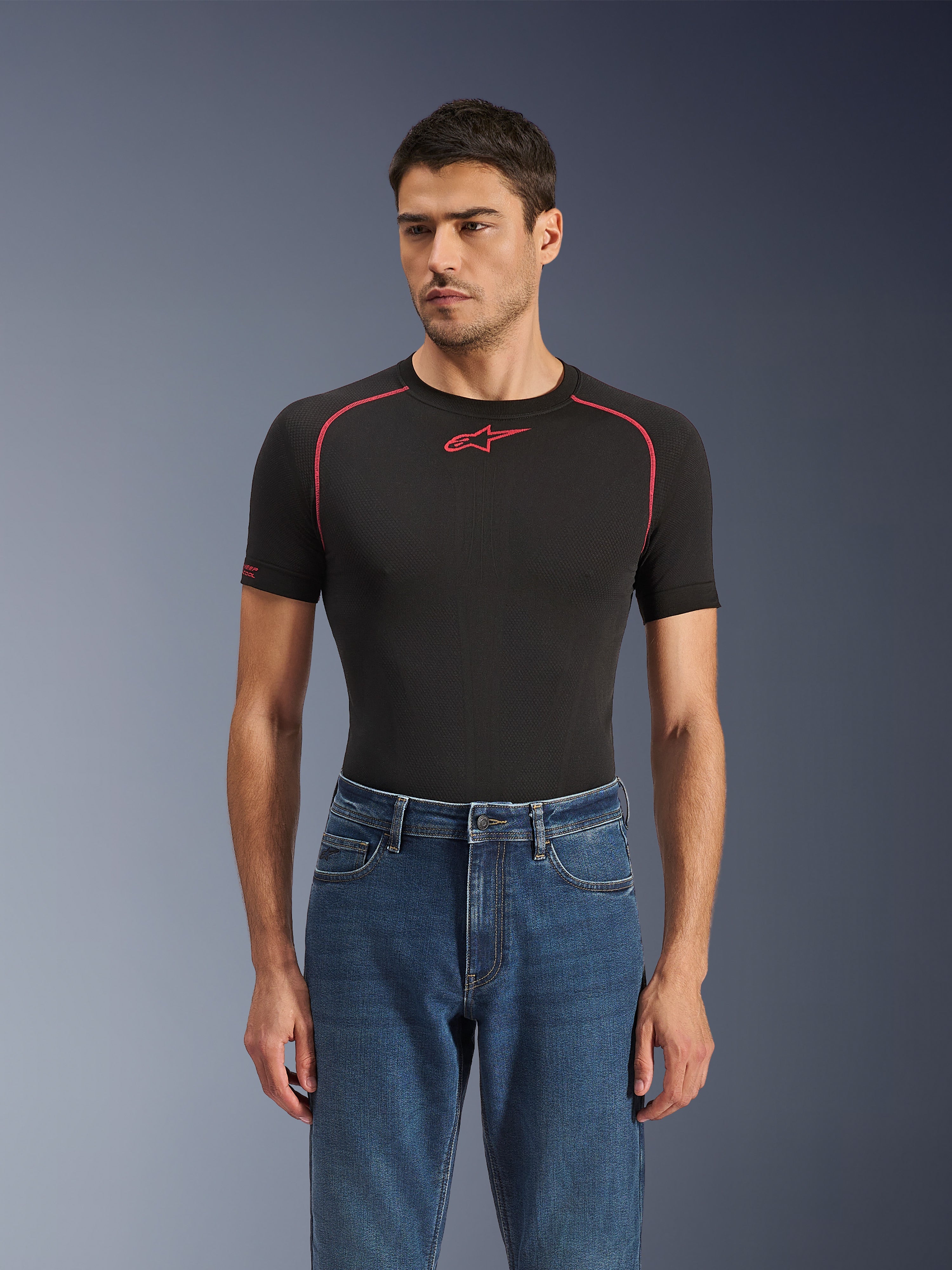 Alpinestars Flex-AST 5 Denim Hose in Indigo Washed, urbane Motorradjeans mit konischer Passform, getragen von einem männlichen Model mit schwarzem, kurzärmeligem Base Layer mit roten Akzenten, lässiges Road-to-Street-Styling