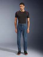 Alpinestars Flex-AST 5 Denim-Hose, Indigo Washed blaue Denim-Motorradhose, reguläre konische Passform, getragen von einem Model mit schwarzem Alpinestars Base Layer und schwarzen Freizeitschuhen, urbane Motorrad-Lifestyle-Bekleidung.