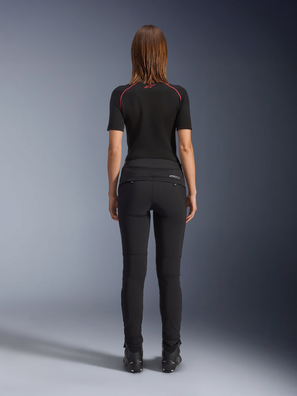 Alpinestars Alamosa Damenhose, Schwarz, Rückansicht mit schmaler Textilkonstruktion, Gesäßtaschen mit Reißverschluss und reflektierendem MO.ST.EQ.-Branding auf der Rückenpasse, getragen mit einer schwarzen kurzärmeligen Basisschicht und schwarzen Motorradstiefeln.